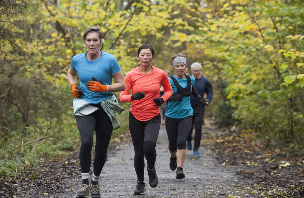 Group of four adults jogging together on a forest trail