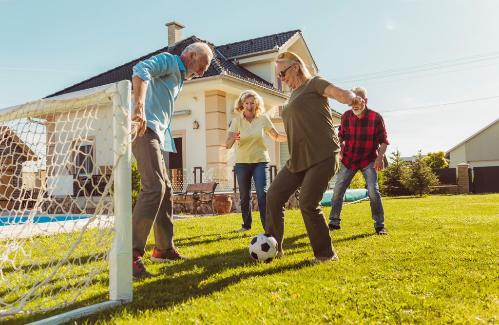 Senior friends having fun playing soccer in the backyard