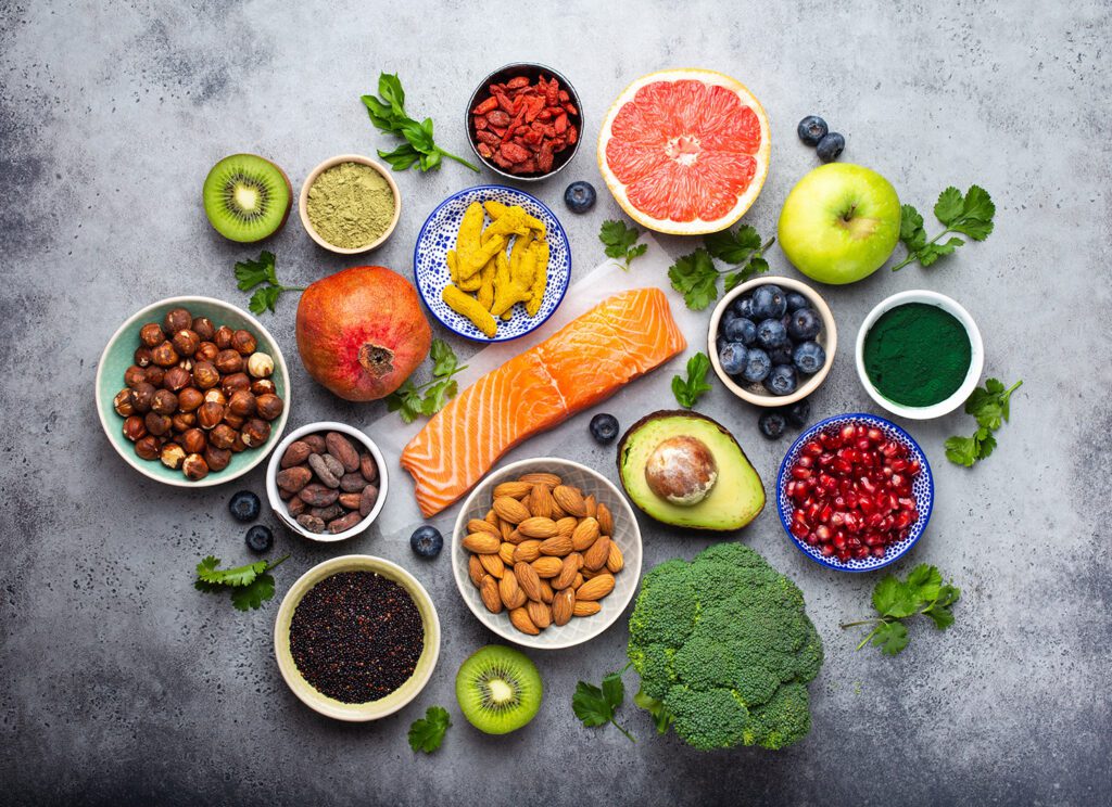 Selection of healthy products and superfoods: salmon, fruit, vegetables, berries, goji, spirulina, matcha, quinoa, chia seeds, nuts.